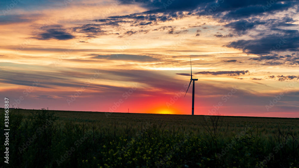 Obraz premium wind generator in grass field at sunset