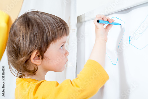 little child draws on a white board with a felt-tip pen. Home activities in self-isolation