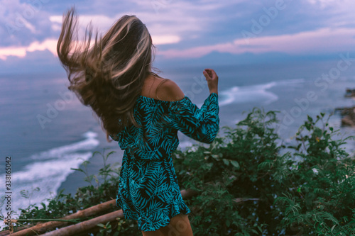 A beautiful girl stands on a cliff overlooking the waves of the blue ocean. Tropical paradise and exotic nature on the island of Bali. Model with different emotions of happiness and joy. photo