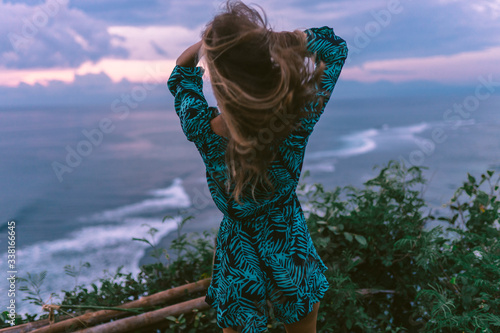 A beautiful girl stands on a cliff overlooking the waves of the blue ocean. Tropical paradise and exotic nature on the island of Bali. Model with different emotions of happiness and joy. photo