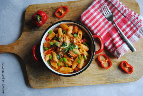 Penne Pasta with Sausages and Peppers sprinkled with Green onions and Parmesan. Served on a wooden kitchen board. Top view.