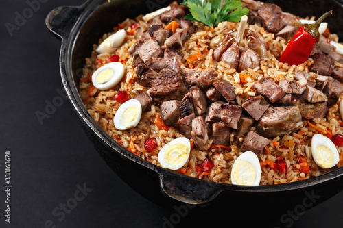 Close-up of pilaf with sliced meat, garlic decorated with quail eggs. Family portion. Uzbek traditional dish plov. Dark background.