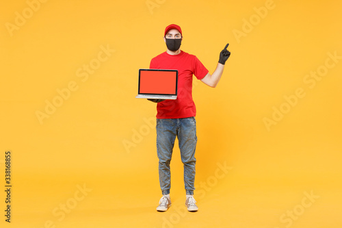 Delivery man in red cap blank t-shirt uniform mask gloves isolated on yellow background studio Guy employee work hold laptop pc computer Service quarantine pandemic coronavirus virus 2019-ncov concept