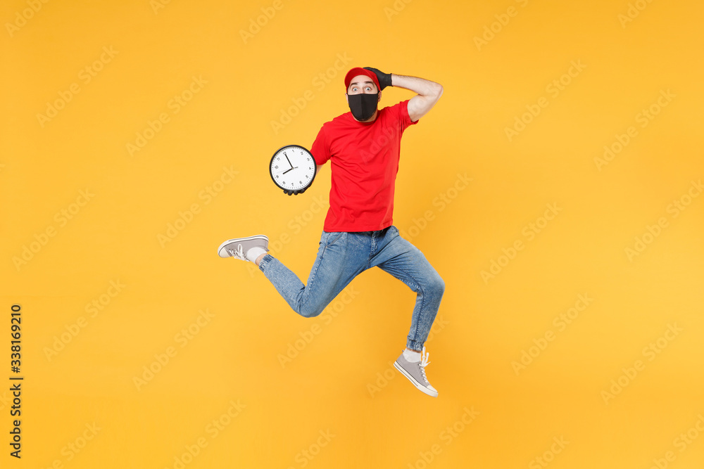 Fun jumping delivery man in red cap t-shirt uniform sterile face mask gloves isolated on yellow background studio Guy employee courier Service quarantine pandemic coronavirus virus 2019-ncov concept. Fun jumping delivery man in red cap t-shirt uniform sterile face mask gloves isolated on yellow background studio Guy employee courier Service quarantine pandemic coronavirus virus 2019-ncov concept.