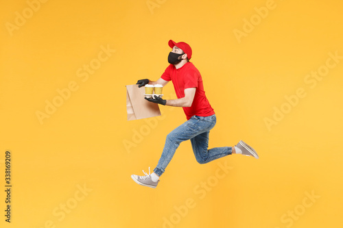 Fun jumping delivery man guy employee in red cap mask gloves hold craft paper packet food coffee isolated on yellow background studio. Service quarantine pandemic coronavirus virus 2019-ncov concept. © ViDi Studio