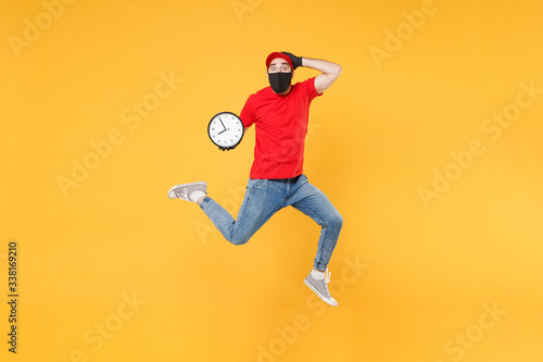 Fun jumping delivery man in red cap t-shirt uniform sterile face mask gloves isolated on yellow background studio Guy employee courier Service quarantine pandemic coronavirus virus 2019-ncov concept. © ViDi Studio