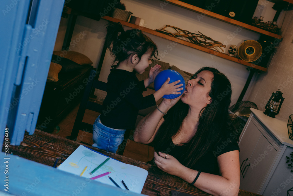 mother and daughter inflating a blue balloon at a wooden desk during the lockdown for covid 19 mother and daughter inflating a blue balloon at a wooden desk during the lockdown for covid 19