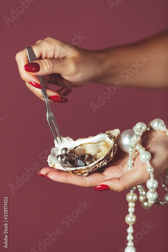 female hand holds oyster shell with pearls from jewelry. It pierces the spit. Concept poster