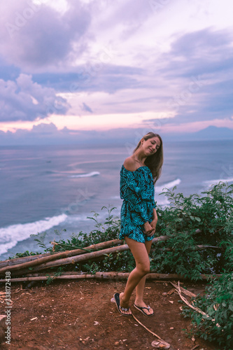 A beautiful girl stands on a cliff overlooking the waves of the blue ocean. Tropical paradise and exotic nature on the island of Bali. Model with different emotions of happiness and joy. photo