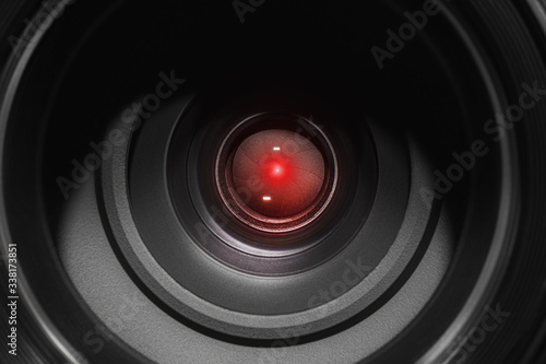 Eye of the camcorder glows red - the concept of video tracking and video monitoring systems. Concept of hidden photo and video shooting, espionage. Camera lens closeup.