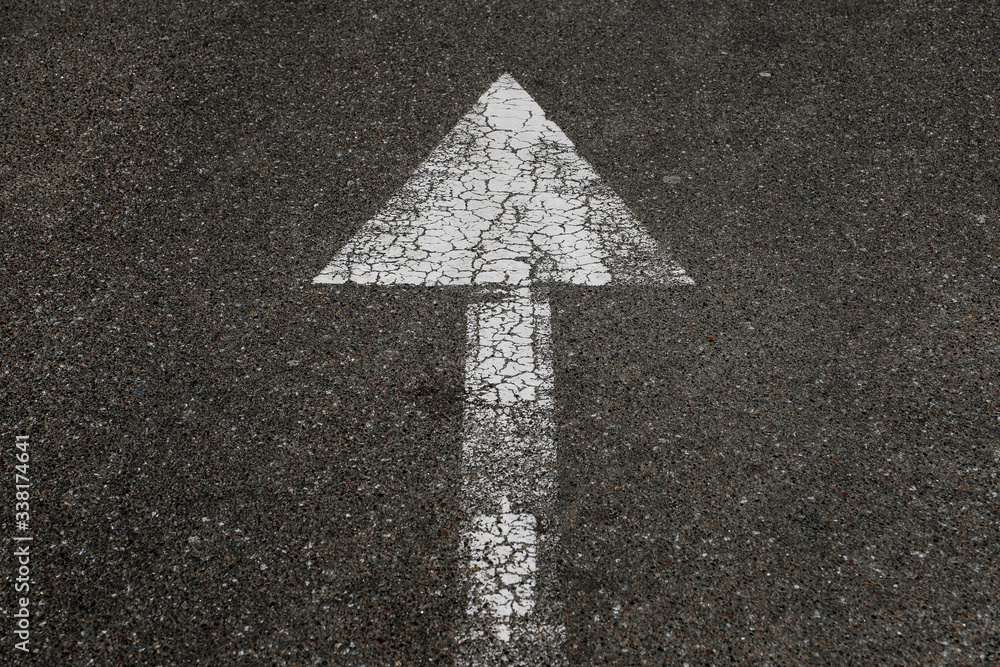 Textured white arrow on the pavement. White street arrow pointing to direction of traffic. Textured white arrow on the pavement. White street arrow pointing to direction of traffic.