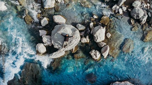 Aerial shot above a man lay down on the rock in blue river New Zealand.