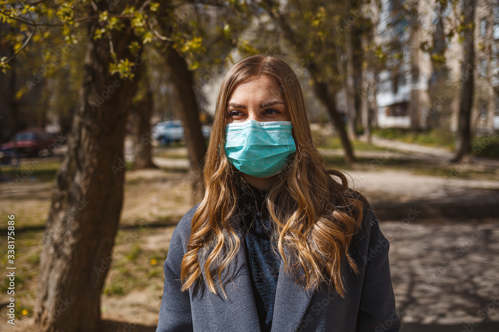 Girl, young woman in a protective sterile medical mask on her face, looking at the camera outdoors, in the spring garden. Air pollution, virus, pandemic coronavirus concept. Girl, young woman in a protective sterile medical mask on her face, looking at the camera outdoors, in the spring garden. Air pollution, virus, pandemic coronavirus concept.