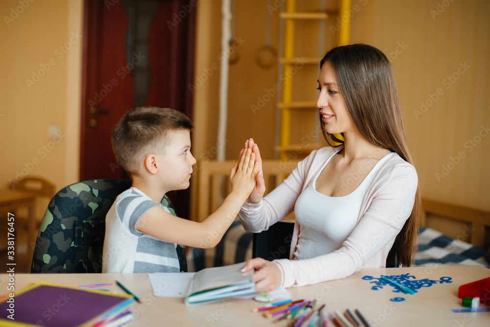Fototapeta premium A young mother is doing homework with her son at home. Parents and training