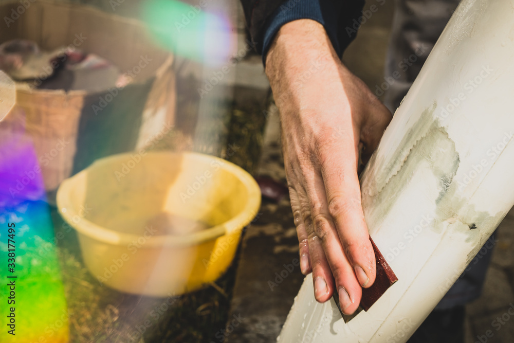 Fototapeta premium Closeup of a man hand wet sanding a model aeroplane or plastic body. Man holding a 80 grit sanding paper and wet sanding a plastic part.