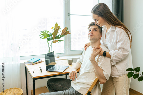 married caucasian couple happy together at home, careful wife and working husband with laptop. woman entertain, talk with him while he is at freelance work from home photo