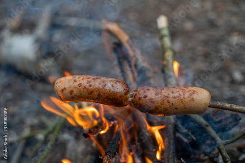 Sausages on a stick are fried on a fire in the forest close up