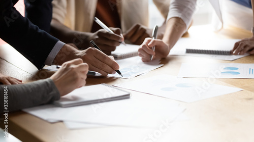 Close up of diverse businesspeople gather at office desk discuss company financial paperwork at meeting together, multiracial colleagues brainstorm work with documents at briefing in boardroom