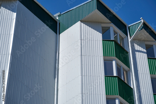 facade of a new multistory building with white and green metal siding, many Windows