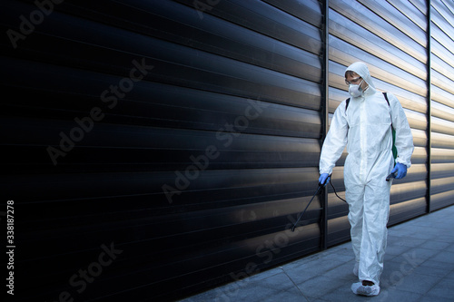 Shot of exterminator person in white chemical protection suit doing disinfection and pest control and spraying poison to kill insects and rodents. Successful pest control and extermination. photo