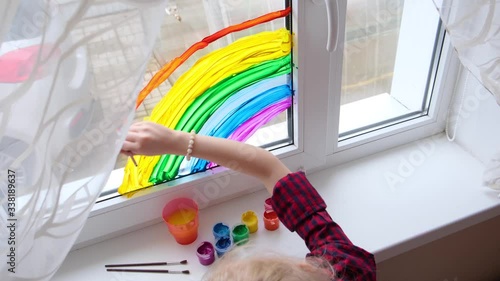 4k. Girl painting rainbow on window during Covid-19 quarantine at home. Stay at home social media campaign for coronavirus prevention, let's all be well, hope. Chase the rainbow. photo
