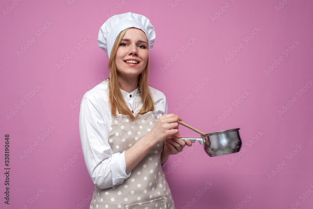 beautiful cheerful girl cook in kitchen clothes holds a pot and cooks dinner on a pink background, woman is a housewife with kitchen items beautiful cheerful girl cook in kitchen clothes holds a pot and cooks dinner on a pink background, woman is a housewife with kitchen items