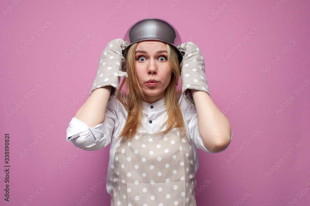 shocked girl cook in kitchen clothes with a pan on her head surprised at a colored background, woman housewife with kitchen items shocked girl cook in kitchen clothes with a pan on her head surprised at a colored background, woman housewife with kitchen items