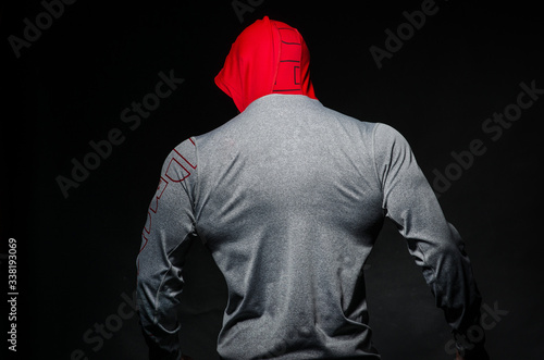 A sporty guy stands in the Studio against a dark background in a hood. Sports, beauty