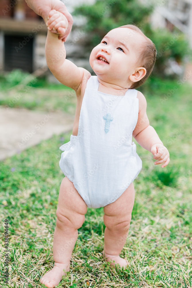 Sweet adorable baby boy looking up and smiling to a person off-camera. He is wearing a cross shaped white onesie outfit, he is barefoot in the grass. Sweet adorable baby boy looking up and smiling to a person off-camera. He is wearing a cross shaped white onesie outfit, he is barefoot in the grass.