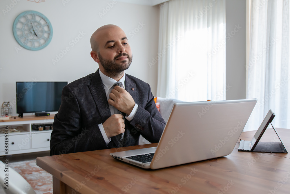 Confident man with young beard who straightens his tie and top while waiting for a job interview with a business leptop at home Confident man with young beard who straightens his tie and top while waiting for a job interview with a business leptop at home