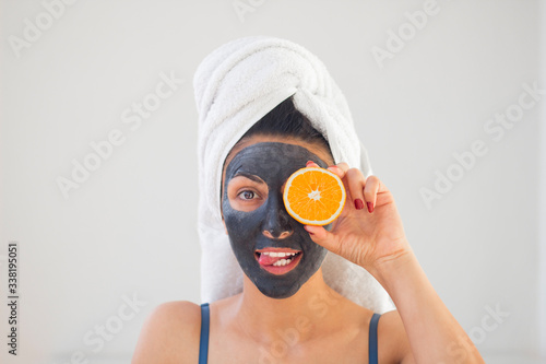 unny girl shows tongue, on face a black cleansing mask and orange fruit photo