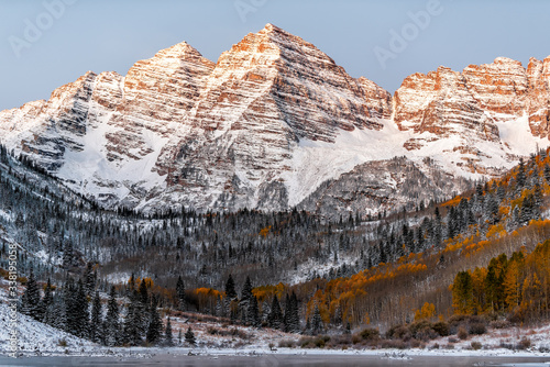 Maroon Bells morning sunrise yellow sunlight on peak in Aspen, Colorado rocky mountain and autumn yellow foliage view and winter snow
