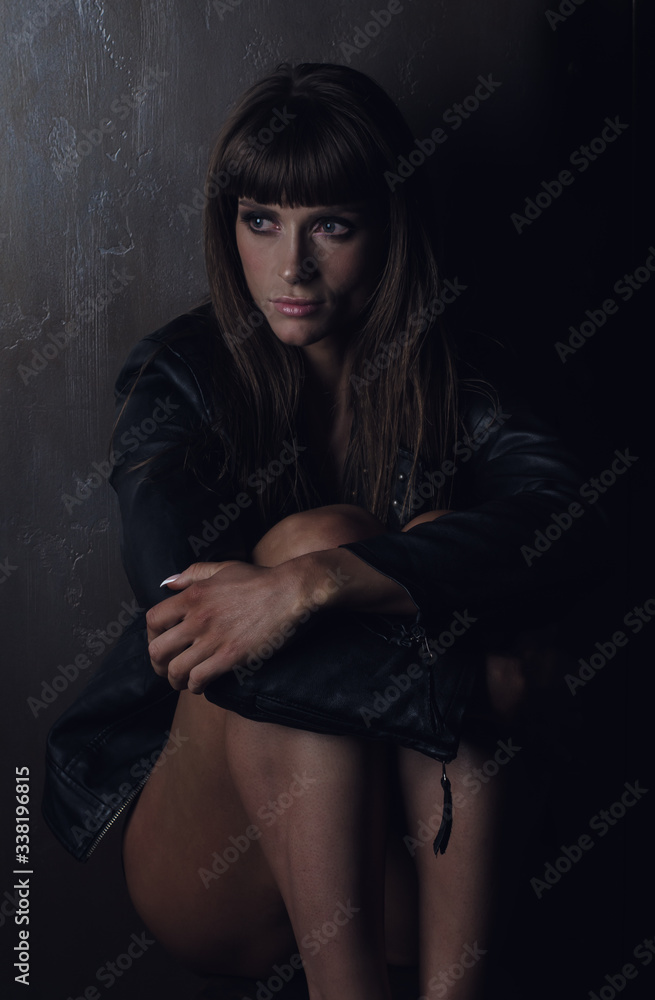 Girl bodybuilder in a black leather jacket closeup posing in a photo studio. A girl showing a trained body shape. Low key style photo