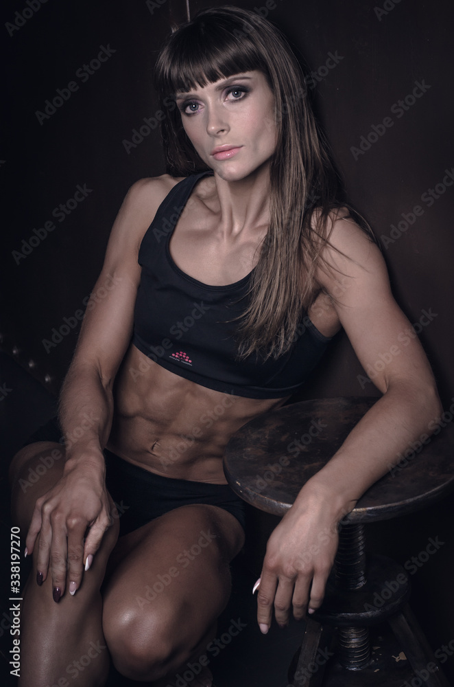 Naklejka premium Girl bodybuilder in a swimsuit closeup posing in a photo studio. A girl showing a trained body shape. Low key style photo.
