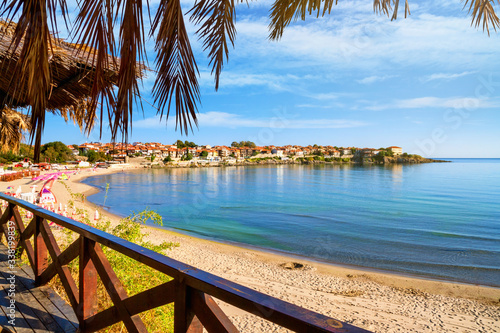 Fototapeta Naklejka Na Ścianę i Meble -  Seaside landscape - view from the cafe to the sandy beach with umbrellas and sun loungers in the town of Sozopol on the Black Sea coast in Bulgaria