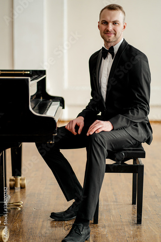 Photo portrait of young pianist in formal elegant suit with bow tie, sitting next to c