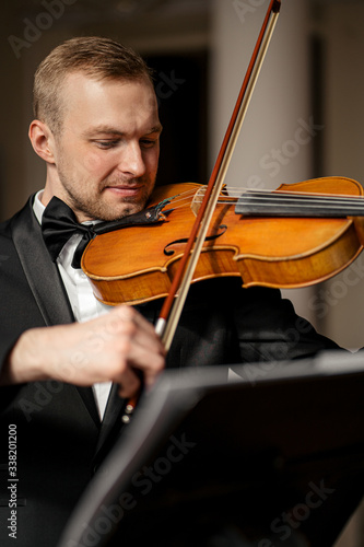 young caucasian handsome guy play violin, talented musician perform music with the use of classical instrument, wearing elegant formal suit, before concert or performance