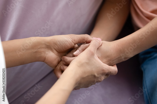 Close up african american mother and teen daughter hand holding together. Caring family spend time in private in living room at home. Young mom and girl create sweet bonding.