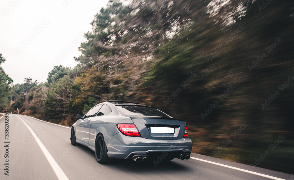 Blue cabriolet with red xenon lights on the forest drive to the left