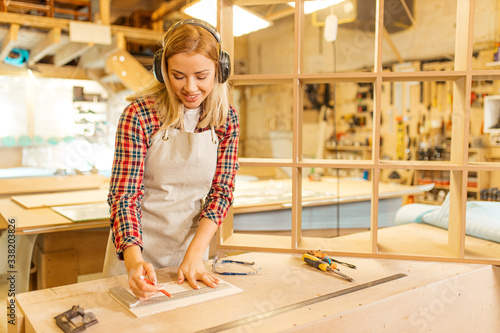 portrait of young caucasian carpenter working in workshop listening to music, woman enjoy making wooden furniture, woman isolate herself from noisy sounds in factory