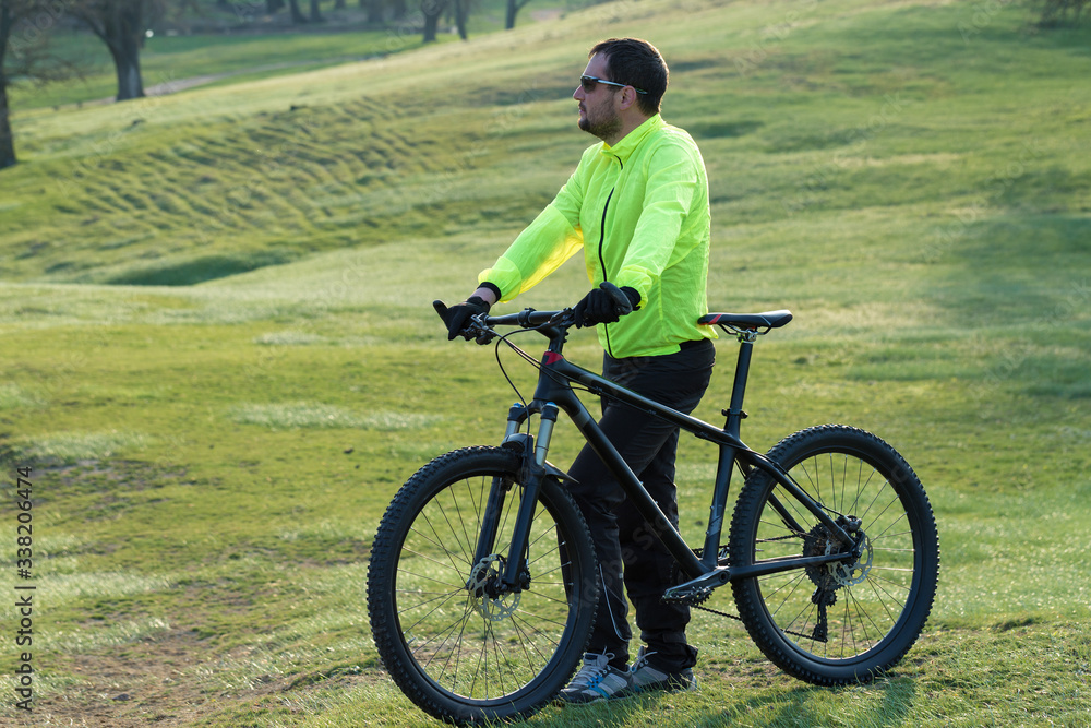 Fototapeta premium Cyclist in pants and green jacket on a modern carbon hardtail bike with an air suspension fork. The guy on the top of the hill rides a bike.