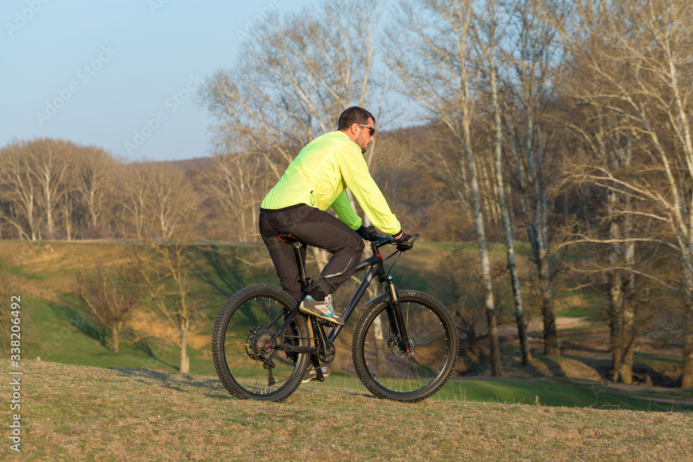 Cyclist in pants and green jacket on a modern carbon hardtail bike with an air suspension fork. The guy on the top of the hill rides a bike. Cyclist in pants and green jacket on a modern carbon hardtail bike with an air suspension fork. The guy on the top of the hill rides a bike.