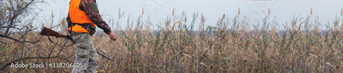 Hunting period, autumn season open. A hunter with a gun in his hands in hunting clothes in the autumn forest in search of a trophy. A man stands with weapons and hunting dogs tracking down the game.