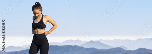 A thin athletic girl takes a break between classes on the background of mountains in the early morning, enjoys silence and freedom.
