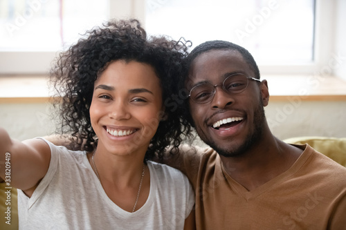 Close up headshot portrait of African American husband and wife taking selfie, smiling woman holding phone, happy man posing for photo with girlfriend, family having fun together with gadget.