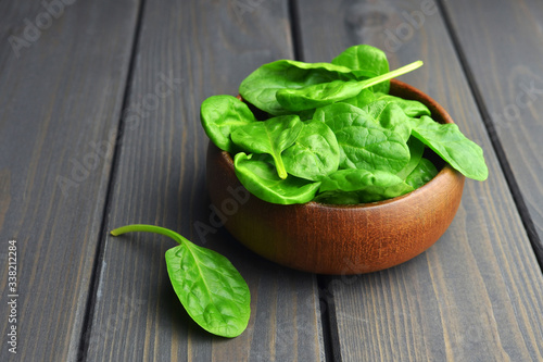 Spinach leaves in wooden bowl on dark wooden table background. Healthy vegan food trend. Vegan lifestyle concept.