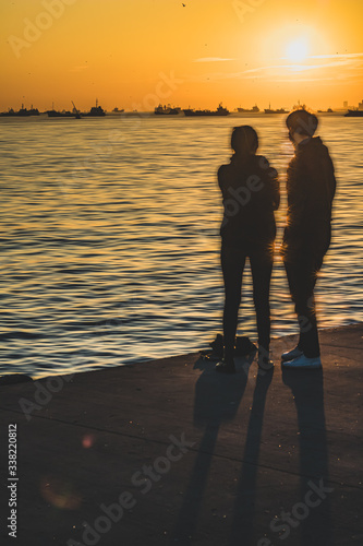 Silhouette of a Couple looking at Waiting Cargo Ships at Sunset Reflection