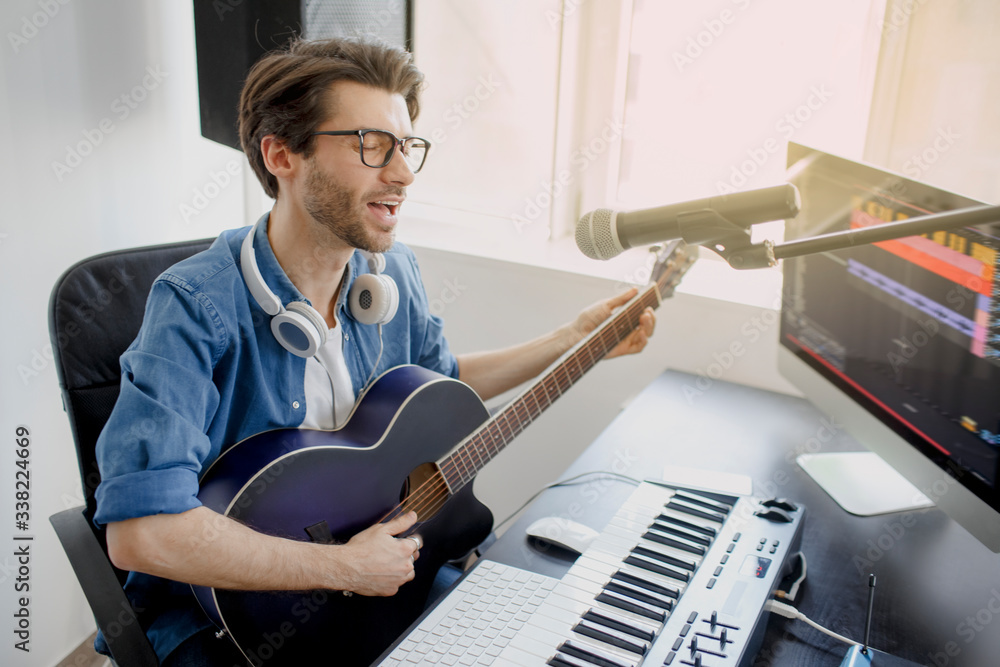 Man plays guitar and singing and produce electronic soundtrack or track in project at home. Male music arranger composing song on midi piano and audio equipment in digital recording studio Man plays guitar and singing and produce electronic soundtrack or track in project at home. Male music arranger composing song on midi piano and audio equipment in digital recording studio