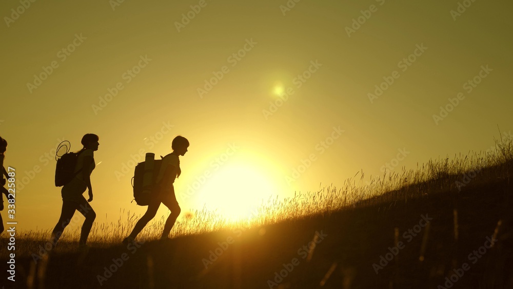 children and mom with backpacks travel climb mountain in sun. mom and daughters go camping. Family of tourists with kids traveling at sunset. joint work of tourists. movement to victory.