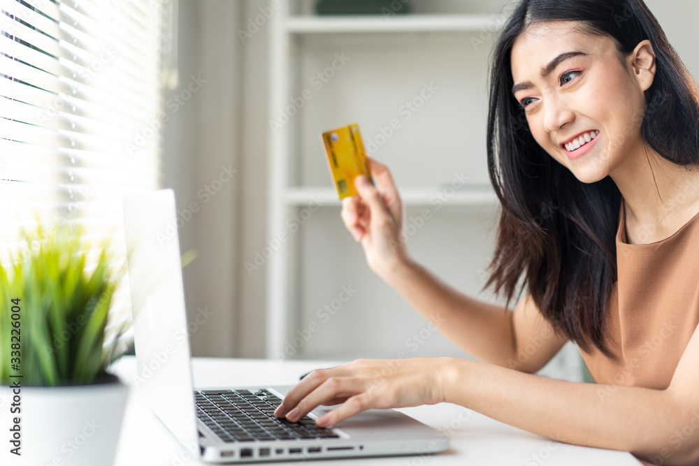 E-commerce and shopping online concept. Asian beautiful girl buying online from website using credit card for payment. She holding credit card in hand sitting at the table at home to order items. E-commerce and shopping online concept. Asian beautiful girl buying online from website using credit card for payment. She holding credit card in hand sitting at the table at home to order items.
